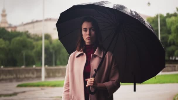 Jeune femme sérieuse debout sous le parapluie sous la pluie, temps triste en ville
 - Séquence, vidéo