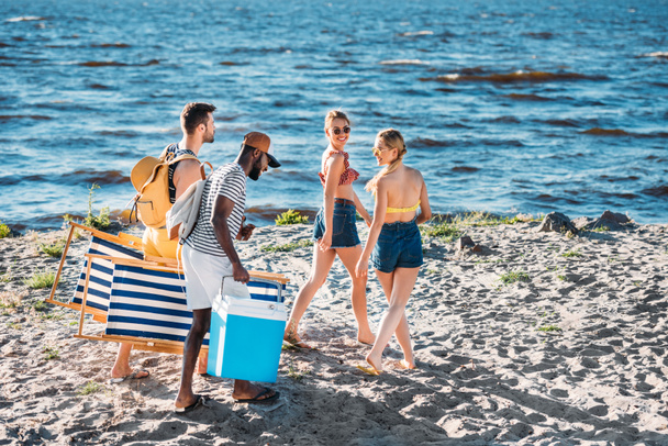 hoge hoekmening van jonge multi-etnisch vrienden, met strand items lopen op zanderige kust  - Foto, afbeelding