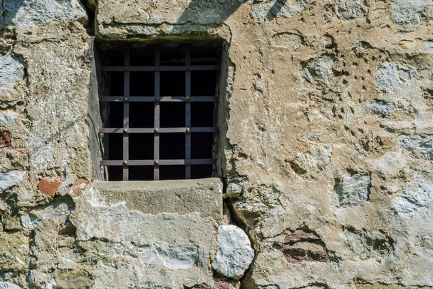 Antigua celda medieval pequeña ventana con barras de metal y pared de ladrillo de roca
 - Foto, imagen