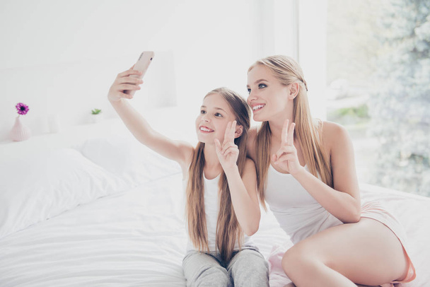 Rest relax lifestyle pajama party daydreaming concept. Pretty careless charming attractive beautiful cute sweet ladies taking making photo on telephone in white light bedroom sitting on bed - Фото, зображення