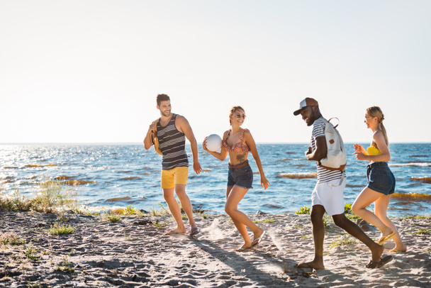 heureux jeunes amis multiethniques avec ballon et sacs à dos marchant ensemble sur la plage de sable
 - Photo, image