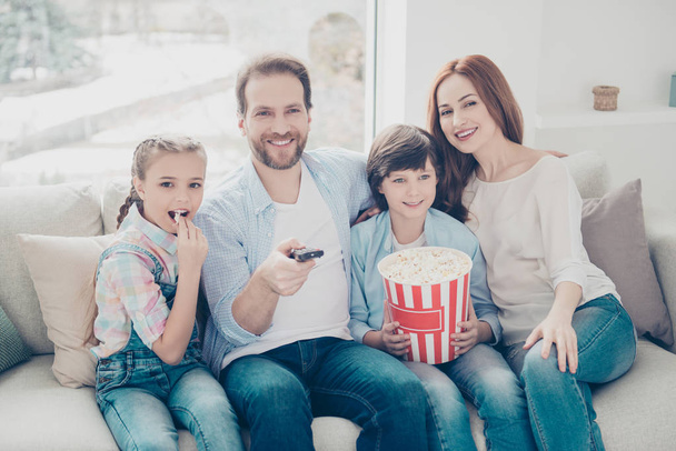 Portrait of joyful mama daddy two kids looking tv sitting on sofa having popcorn in hands using console searching favorite program enjoying comedy. Domestic lifestyle concept - Foto, imagen
