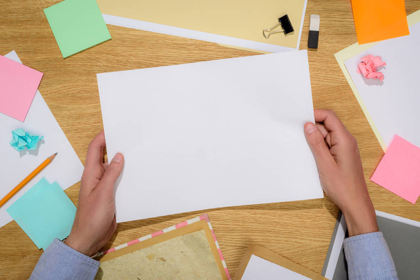 cropped image of woman holding empty white paper over table with stationery supplies  - Photo, Image