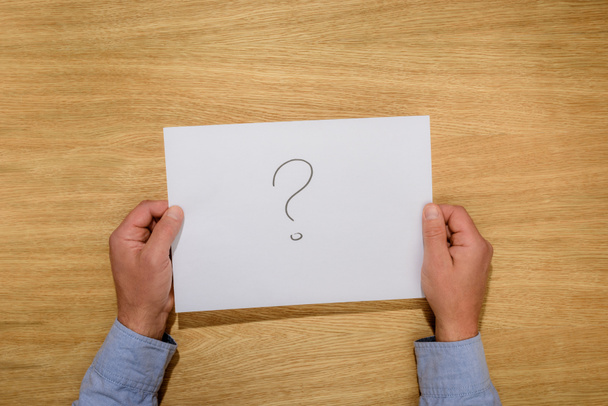 cropped image of man holding paper with question mark over wooden table  - Photo, image