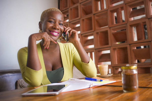 young elegant and beautiful black African American business woman working online with mobile phone at coffee shop smiling happy in entrepreneur success and internet freelance job concept - Photo, Image