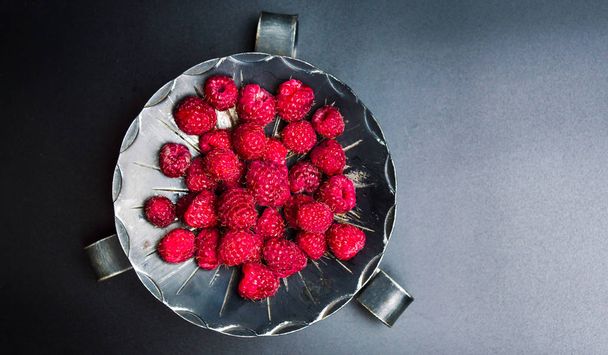 Raspberry fruits on a dark bowl top view - Foto, afbeelding