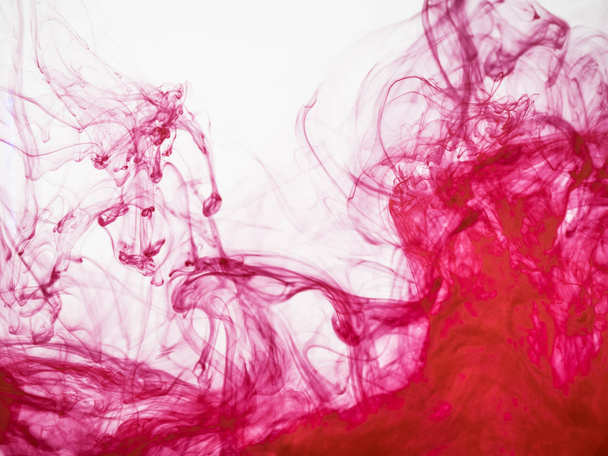 Abstract red coloured background. Image of frozen red coloured flow of paint in water. Droplet of acrylic paint dropped in liquid and photographed while in motion. Red ink transforming into water. - Zdjęcie, obraz