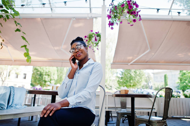 African american girl wear in glasses with mobile phone sitting at outdoor caffe. - Foto, Imagem