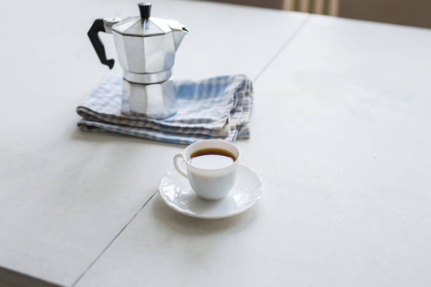Чашка кави, кавовий чайник на білому столі
 - Фото, зображення