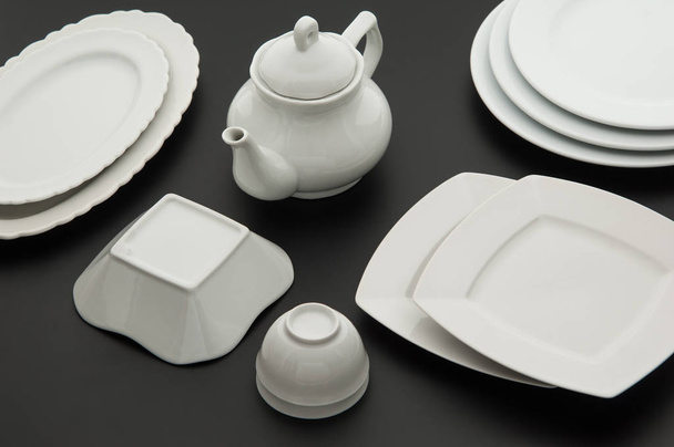 set of kitchen white ceramic tableware on black background, top view - Фото, изображение