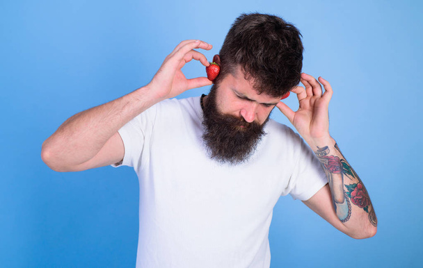 Man bearded hipster red ripe strawberry ears as headphones. Summer hit concept. Hipster beard listen music strawberry earphones. Guy enjoy juicy sound summer hit song music. Summer playlist music - Fotografie, Obrázek
