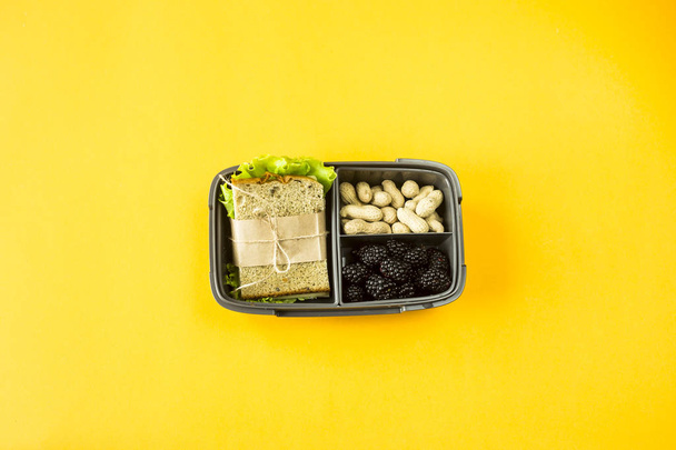 Lunchbox with food - sandwich, nuts and berries on a yellow background. Top view, flat lay,  - Photo, Image