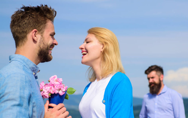 New love. Ex partner watching girl starts happy love relations. Ex husband jealous on background. Couple in love dating outdoor sunny day, sky background. Couple with flowers bouquet romantic date - Foto, afbeelding