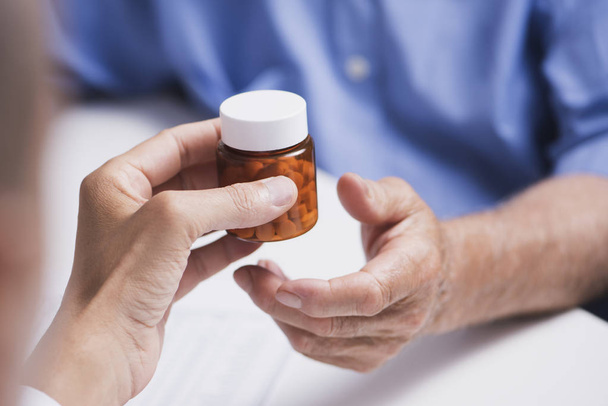 Close-up van een Kaukasische arts man, in een witte jas, een fles pillen geven een hoge Kaukasische patiënt man, zit zowel aan de balie van een artsen - Foto, afbeelding