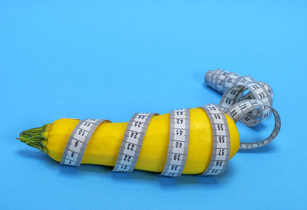 yellow raw zucchini wrapped in a measuring tape on a blue background, concept of losing weight and healthy lifestyle - Photo, Image