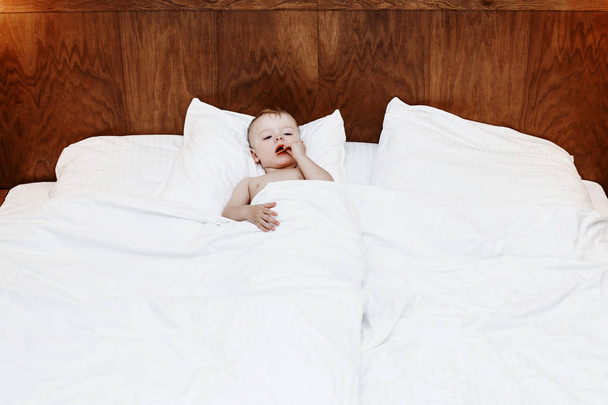 A gyermek is az ágyban. Fiú-nagy ágyon, a takaró és a párna között. Egy kis baba ült az ágyban, és eszik. A gyermek, aki she\ a indulging. - Fotó, kép