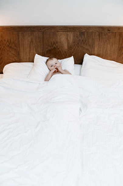 das Kind liegt im Bett. Junge auf einem großen Bett zwischen einer Decke und einem Kissen. Ein kleines Baby sitzt im Bett und isst. das Kind, das sich verwöhnt. - Foto, Bild