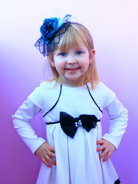 Маленькая девочка в модной шляпе улыбается и позирует на сиреневом фоне. Детские позитивные эмоции. Выражение веселья. Детская мода. Концепция моды. Лицо
 - Фото, изображение