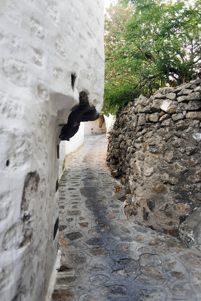 Una vista de una calle estrecha con arco y ventanas de madera y puertas con la arquitectura de piedra pared blanca de la isla de Patmos, Grecia
 - Foto, imagen