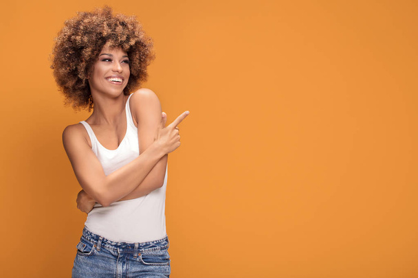 Colorful photo of smiling beautiful african american woman points her finger at the yellow background. - Foto, Bild