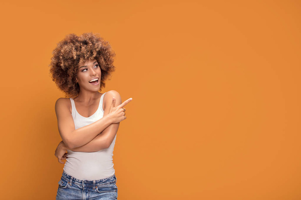 Colorful photo of smiling beautiful african american woman points her finger at the yellow background. - Φωτογραφία, εικόνα