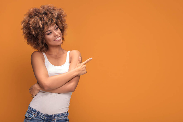 Colorful photo of smiling beautiful african american woman points her finger at the yellow background. - Foto, afbeelding