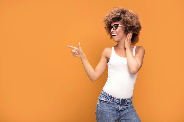 Colorful photo of smiling beautiful african american woman points her finger at the yellow background. - Valokuva, kuva