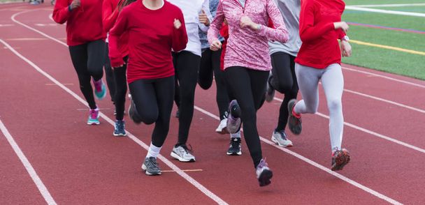 Un cross country del liceo e squadre di atletica corrono insieme in un gruppo su una pista rossa durante le prove
. - Foto, immagini