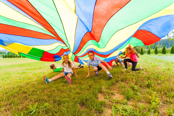Smiling boy and girl under colorful parachute - Фото, изображение