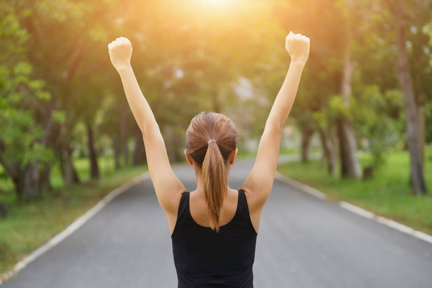 Успешная женщина поднимает руки после перекрестного бега на летнем закате. Фитнес-спортсменка с оружием в руках празднует успех и цели после спортивных упражнений и тренировок
. - Фото, изображение