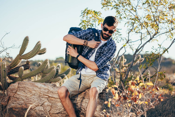 Male hiker putting on a backpack in the desert - Zdjęcie, obraz