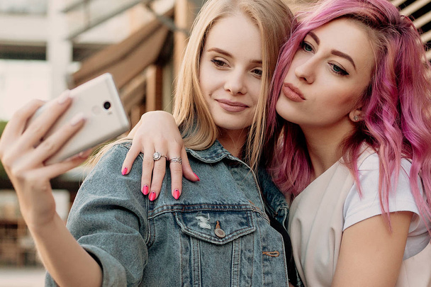 Friends taking selfie with a smart phone and making faces and fun. Closeup of girls making funny faces and smiling for selfie. Two happy girlfriends taking photo with their smartphone in the city - Valokuva, kuva