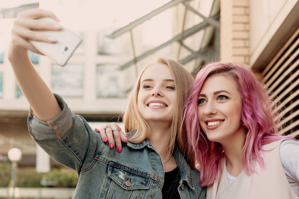 Friends taking selfie with a smart phone and making faces and fun. Closeup of girls making funny faces and smiling for selfie. Two happy girlfriends taking photo with their smartphone in the city - Valokuva, kuva
