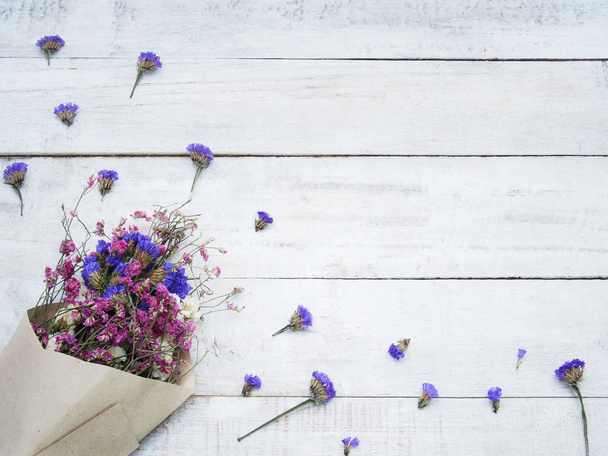 Ramo de flores secas rosa y violeta en papel marrón sobre fondo de madera con espacio para copiar, plano, vista superior
. - Foto, Imagen