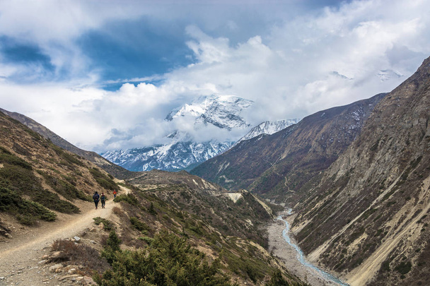 Τουρίστες σε ένα πανέμορφο ορεινό μονοπάτι στα Ιμαλάια. Χιονισμένες κορυφές στα σύννεφα, Νεπάλ. - Φωτογραφία, εικόνα