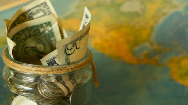 旅行予算の概念。世界地図背景にガラスの瓶に休暇のためお金を保存 - 映像、動画