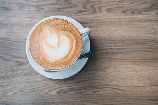 Vue du dessus du café chaud Latte dans une tasse blanche avec latte art sur fond de table en bois
. - Photo, image