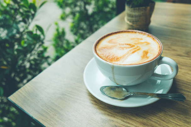 Koffie latte art met kleine boom op de houten bureau in de coffeeshop vintage kleurtoon - Foto, afbeelding