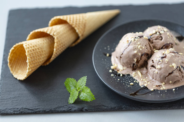 Шоколадное мороженое и вафельный рог на черной тарелке на деревянном столе
 - Фото, изображение