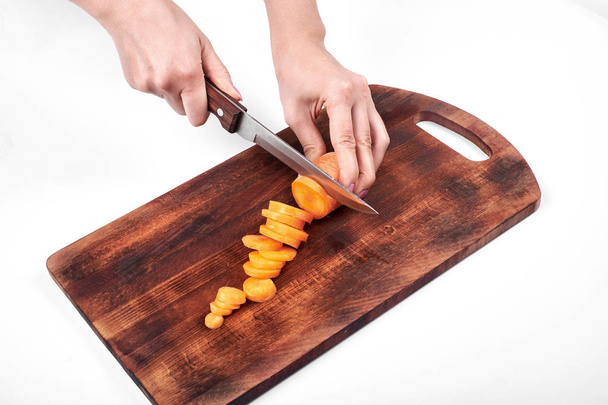 Closeup of woman cooks hands, slicing the carrot on a wooden board, isolated on white background - Photo, Image