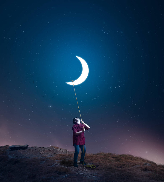 niño arrastra la luna hacia él con una cuerda en medio de la noche. El concepto de cumplir sus sueños
 - Foto, imagen