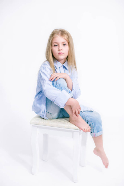 Beautiful fashionable little girl with blond hair in jeans clothes on a white background in studio - Photo, image