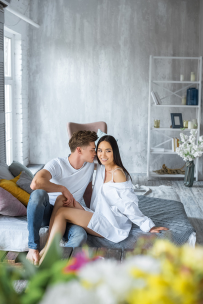 young multicultural couple sitting on bed in morning in bedroom - Foto, afbeelding