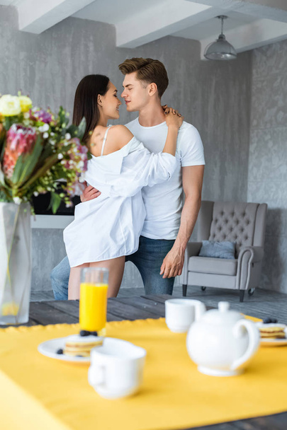 selective focus of breakfast on table and multiracial couple in love hugging at home - Φωτογραφία, εικόνα