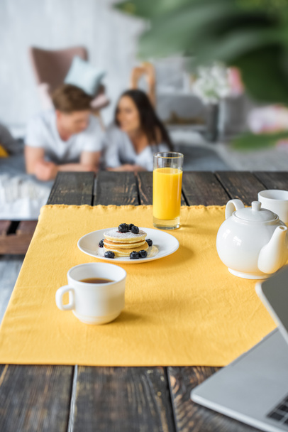 selective focus of breakfast on table and couple in love lying on bed in bedroom - Zdjęcie, obraz