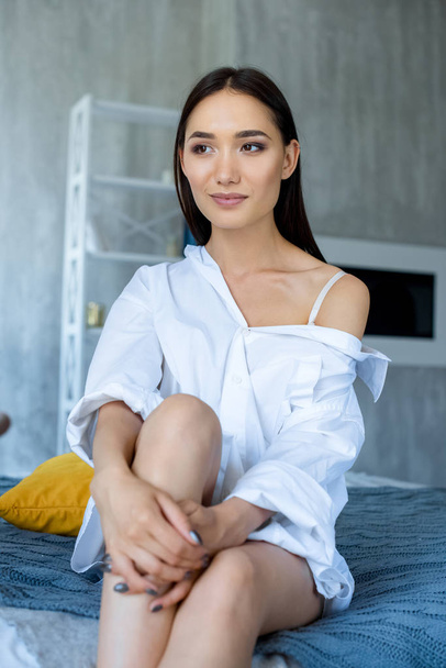 portrait of pensive asian woman in white shirt resting on bed at home - Foto, afbeelding