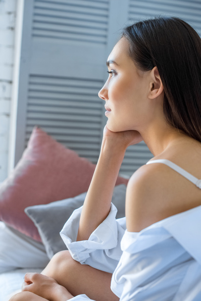 side view of pensive asian woman in white shirt resting on bed at home - Photo, Image
