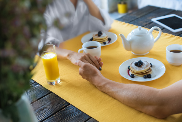 cropped shot of couple holding hands while having breakfast together at home - Foto, Imagem
