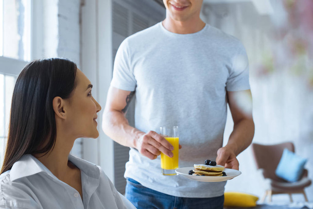 plan recadré de l'homme a apporté le petit déjeuner à petite amie asiatique en chemise blanche à la table à la maison
 - Photo, image