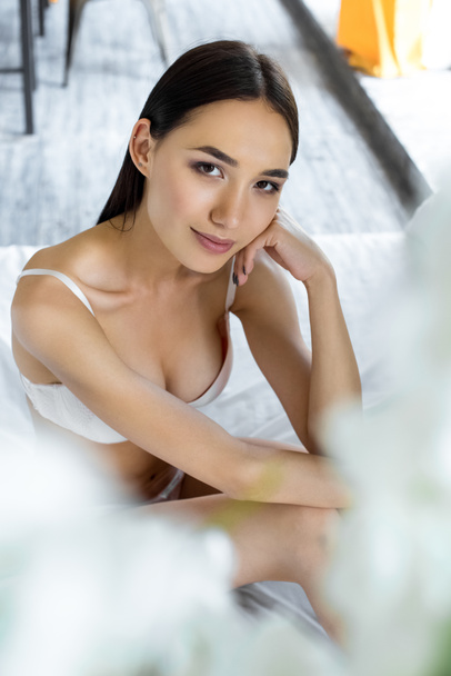 Portret van aantrekkelijke Aziatische vrouw in ondergoed camera kijken op bed - Foto, afbeelding